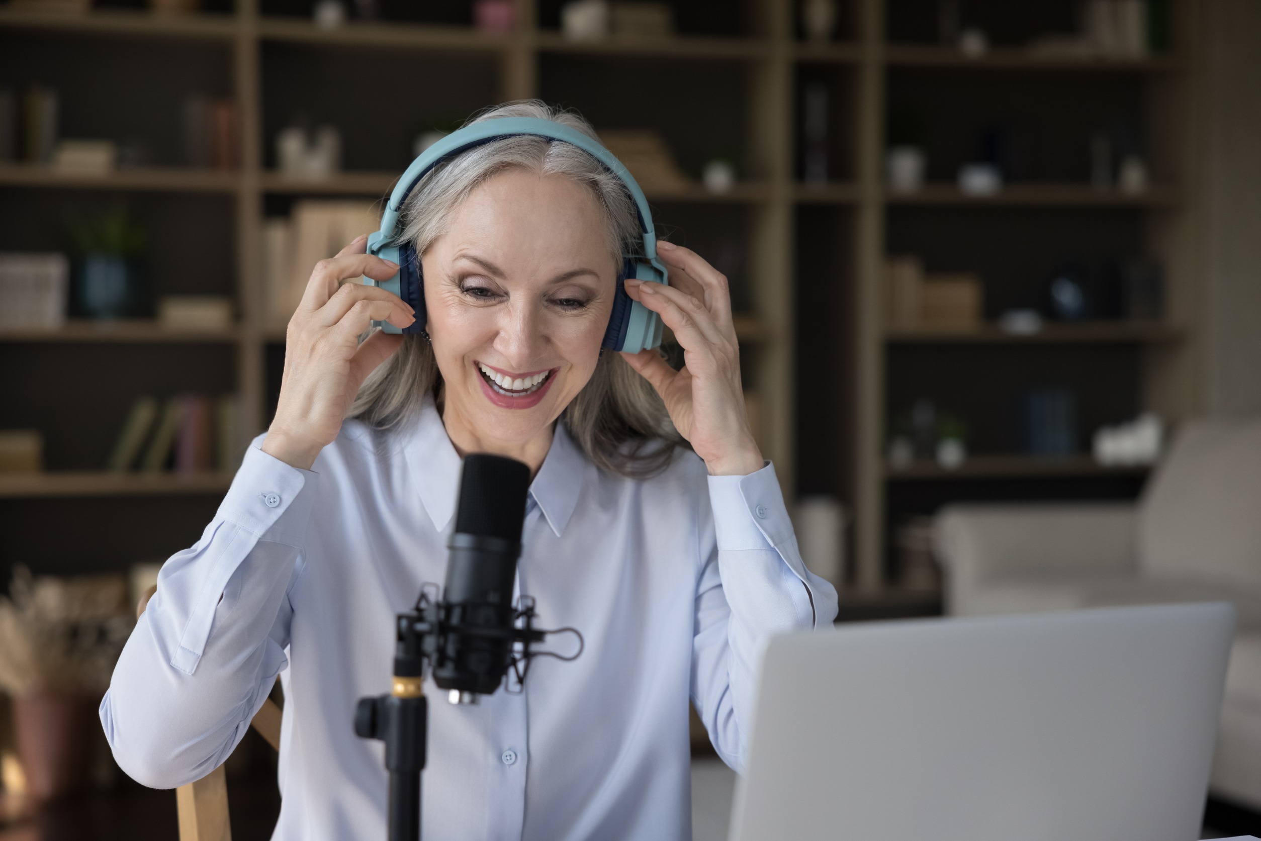 Mature woman hosting a podcast using a microphone and headphones.